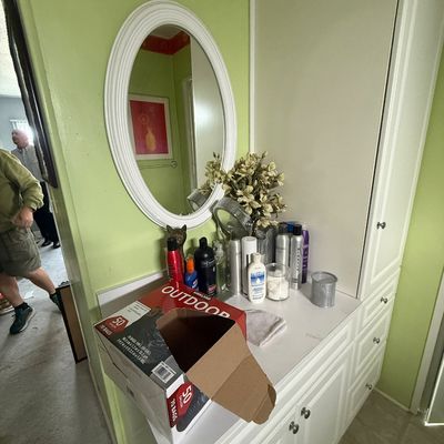 White built-in bathroom vanity with drawers and cabinets, an oval wall mirror, and various personal care products.