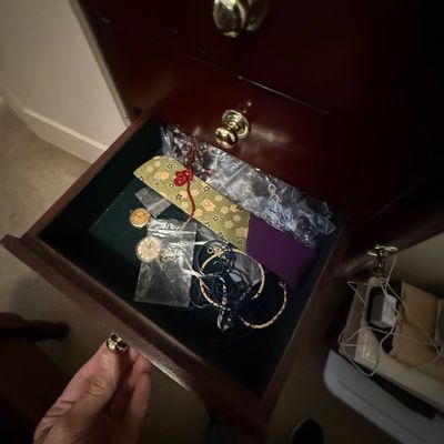Open wooden dresser drawer containing various small jewelry items, watches in plastic baggies, and fabric pouches.