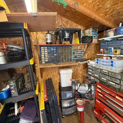 Workshop corner featuring a bench grinder on a pedestal, a router table, multi-drawer hardware organizers, and various power tools.