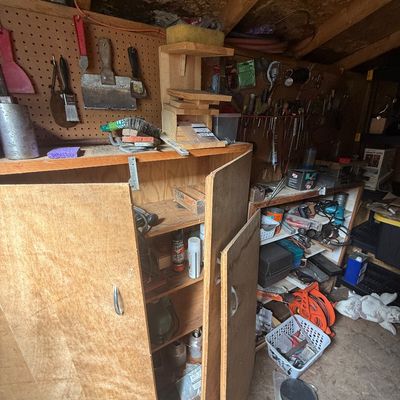 Workshop storage cabinet filled with various tools, hardware supplies, and chemicals, set alongside pegboards and shelving.
