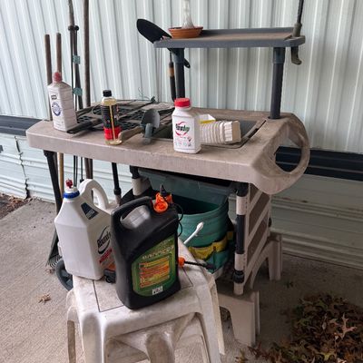 Plastic outdoor potting bench cart filled with assorted lawn and garden tools, hand sprayers, and chemicals.