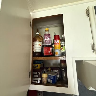 Open white upper kitchen cabinet filled with various pantry items, including cooking spray, syrup, vinegar, and Hershey's cocoa.