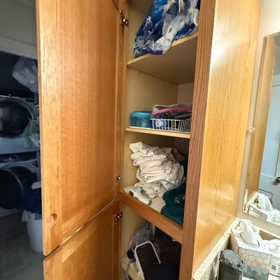 Tall oak bathroom storage cabinet filled with linens and toiletries, installed next to a granite vanity.