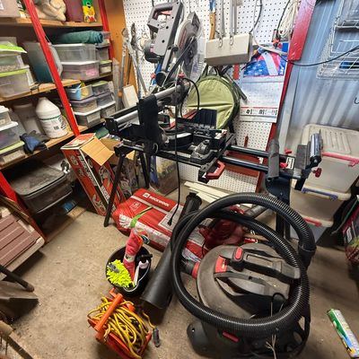 Craftsman sliding compound miter saw mounted on a folding stand, accompanied by a wet/dry shop vacuum and various workshop tools.