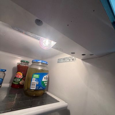 Interior view of an illuminated refrigerator featuring glass shelves holding jarred foods like pickles and salsa.