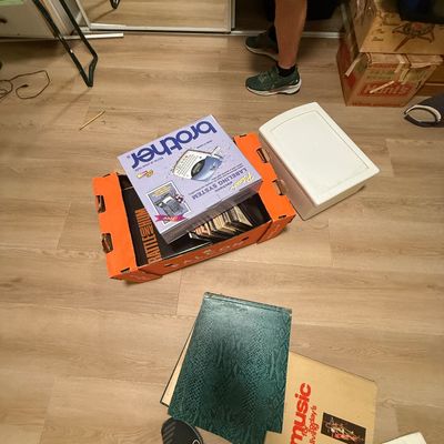 Collection of various estate sale items on the floor, including a boxed vintage Brother P-Touch electronic labeling system, vinyl records...