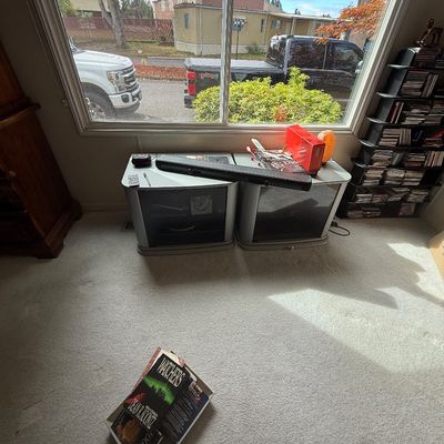 A pair of silver media cabinets positioned under a large window, topped with a black soundbar, salt lamp, and misc items, alongside a...
