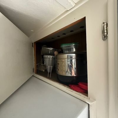 Assorted kitchenware stored in an upper cabinet, including a vintage Sunbeam electric fryer, metal colanders, and plastic storage...