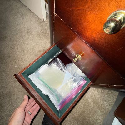 Open drawer of a mahogany finished wooden cabinet, revealing felt lining and plastic bags containing items inside.