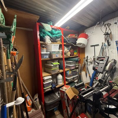 Workshop space packed with assorted power tools, long-handled lawn implements, a red wooden storage unit filled with plastic containers,...