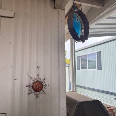 Hanging wire and mesh fish-shaped bird feeder alongside a copper-toned sun face wall ornament.