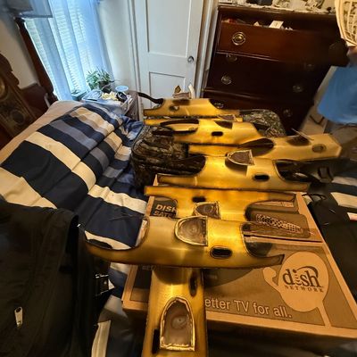 Collection of decorative gold-toned mask-like sculptures, displayed across boxes and luggage on a bed.