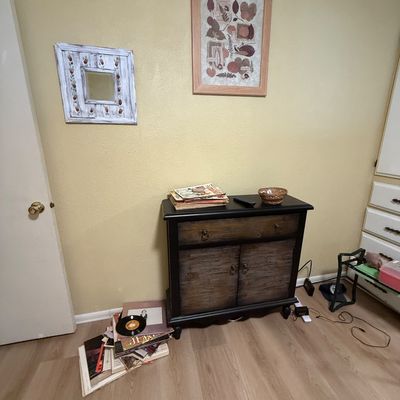 Rustic two-tone black and distressed wood accent cabinet alongside vinyl records, framed wall art, and a rustic mirror.