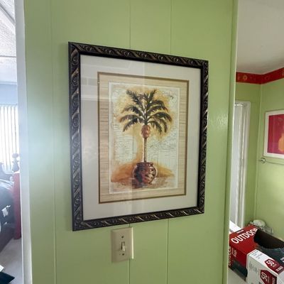 Framed tropical palm tree art print featuring a potted palm against a map background, housed in a textured dark bronze-tone frame.