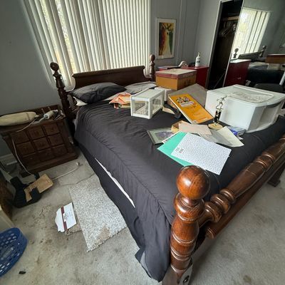 Traditional wooden four-poster bed frame filled with various household items, stationery, and storage boxes alongside a matching nightstand.