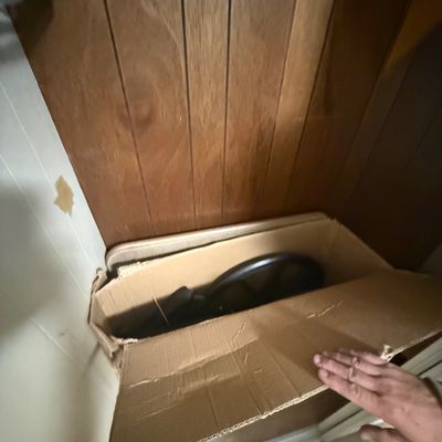 Folded transport wheelchair stored inside an open cardboard box in a closet.