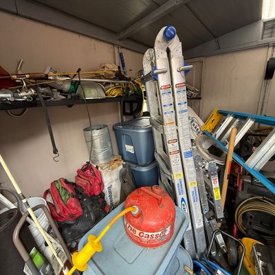 A collection of workshop and yard items inside a shed, including a Werner aluminum multi-position ladder, plastic storage totes, fishing...