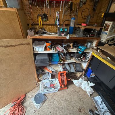 Workshop workbench area filled with various hand tools, power tools, extension cords, and hardware storage.