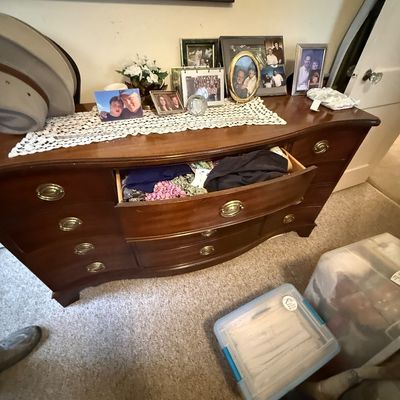 Traditional mahogany serpentine-front dresser with brass bail handles, decorated with framed family photos and a lace runner on top.