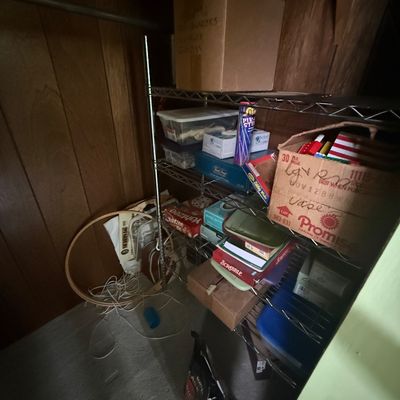 Wire shelving unit inside a closet, filled with vintage board games, cardboard storage boxes, and plastic tote containers.