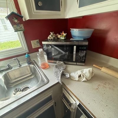 Kitchen countertop setup featuring a stainless steel modern microwave, a wooden rolling pin, plastic bowls, and decorative figurines.