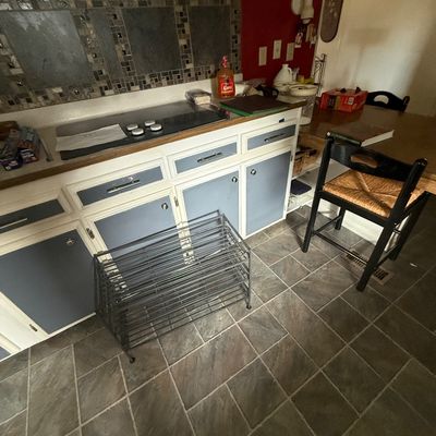 Metal multi-tier shoe rack resting on a tiled kitchen floor near painted two-tone cabinets.