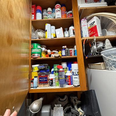 Workshop storage cabinet packed with various household chemicals, spray paints, adhesives, and hardware accessories, situated above a...
