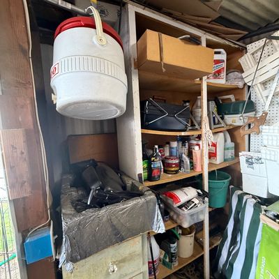 Workshop shelf setup loaded with various tools, cleaning products, automotive supplies, and a hanging Igloo water jug.