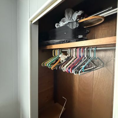 Open closet with wood paneling containing empty plastic clothes hangers, luggage, and a vintage wooden tennis racket on the top shelf.