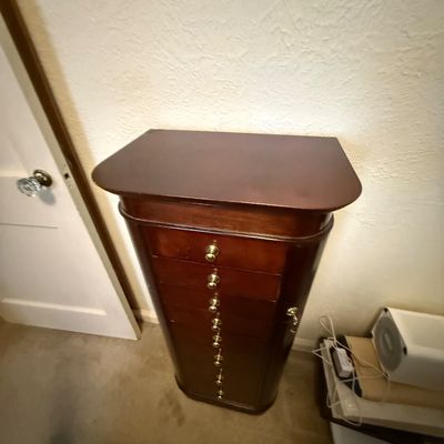 Tall freestanding mahogany jewelry armoire with multiple drawers and brass knobs.