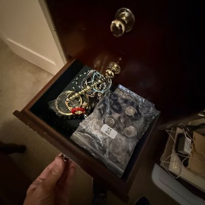 Open wooden furniture drawer containing assorted costume jewelry and bagged items.