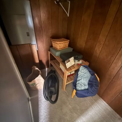 Small wooden slatted shoe rack holding storage boxes and a woven basket, paired with a shop vacuum and duffel bag inside a wood-paneled...