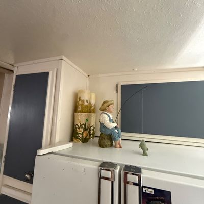 Vintage resin figurine of a young boy in overalls fishing, displayed on top of a refrigerator alongside floral ceramic pillars.
