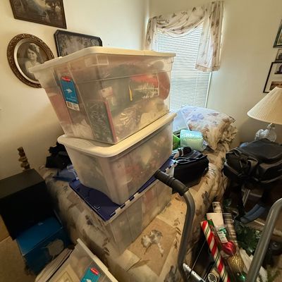 Stack of clear plastic storage bins filled with household goods and holiday decorations resting on a bed.