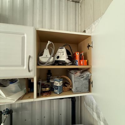 Open laundry room wall cabinet containing a Reliable brand steam iron, Terro ant bait, Shinola shoe polish, and miscellaneous laundry...
