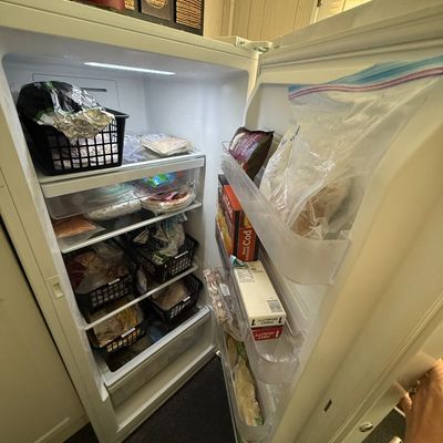 White upright standalone freezer filled with organized food items and door shelf storage.
