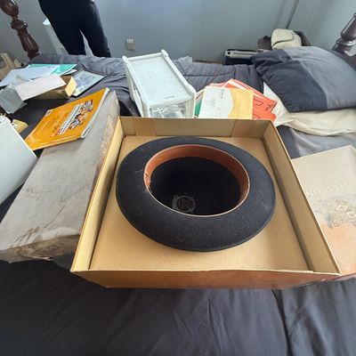 Vintage black Stetson felt hat stored inside its original cardboard hat box, resting on a bed.