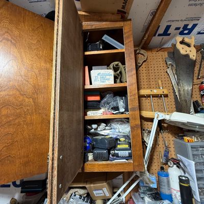 Wall-mounted wooden workshop cabinet with open door revealing shelving packed with small tools, hardware, and supplies.
