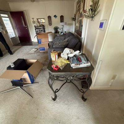 Living room area featuring a wrought iron end table with a tiled top, a dark gray upholstered sofa, and various cardboard packing boxes.