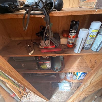 Assorted power tools, aerosol cans, staple gun, and vintage metal toolboxes stored on wooden workshop shelving.