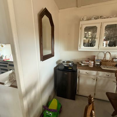 Compact modern Whirlpool mini fridge shown alongside a green plastic ride-on toy and a wall-mounted wooden frame mirror.