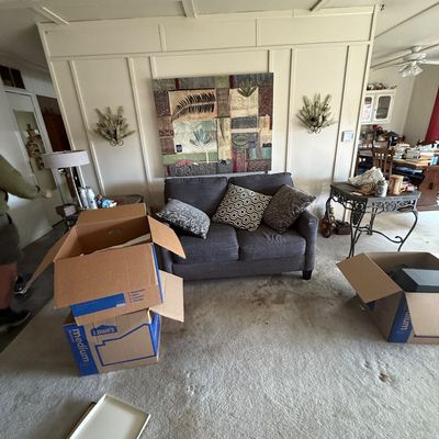 Contemporary charcoal gray upholstered loveseat flanked by wall sconces and art, set alongside packed moving boxes and side tables.