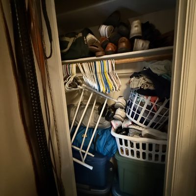 Closet packed with assorted household goods, including plastic storage totes, laundry baskets, shoes, clothes hangers, and a folding...