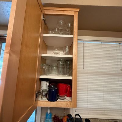 Open wooden kitchen cabinet filled with various glassware, wine goblets, drinking glasses, and coffee mugs.