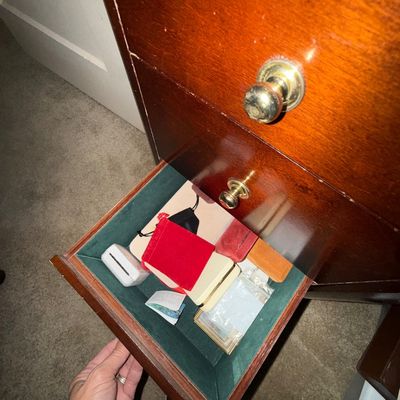 Open felt-lined drawer of a cherry or mahogany nightstand containing small jewelry pouches and trinket boxes.