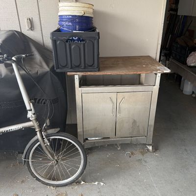 Dahon folding bicycle alongside a rolling stainless steel cart with a wood top, topped with plastic crates and buckets.