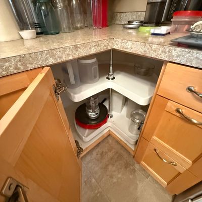 Open corner kitchen cabinet with a two-tiered Lazy Susan, featuring assorted plastic containers, small kitchen appliances, and glass jars...