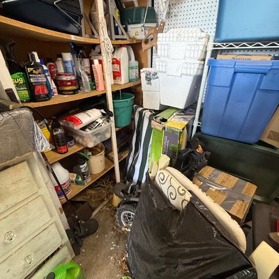 Garage storage area packed with automotive cleaning supplies, plastic totes, folded patio chairs, and miscellaneous tools.