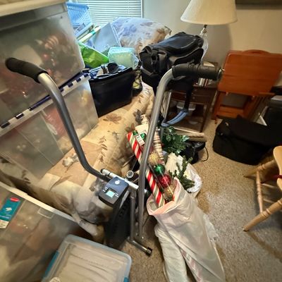 A Gazelle freestyle glider exercise machine positioned in a room alongside storage bins, wrapping paper, and household items.
