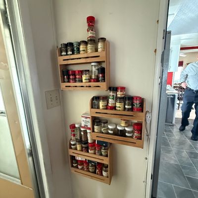Set of three wall-mounted wooden spice racks filled with various spice jars and seasonings.